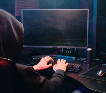 a hacker types on a computer with lines of code on a monitor screen